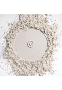 Poudre blanche fine étalée en cercle avec un centre dégagé et lisse et une petite spirale en relief au milieu sur une surface blanche.