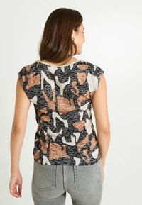 Camiseta de manga corta con un patrón abstracto en negro, blanco y marrón. Tela suave y ligera con un cuello redondo y un corte holgado.