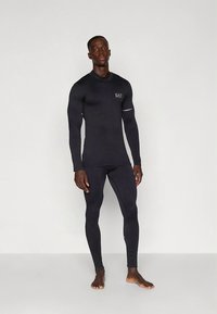 Top sportivo a maniche lunghe e leggings neri in materiale elasticizzato. Presentano una vestibilità aderente e un piccolo logo sul petto.