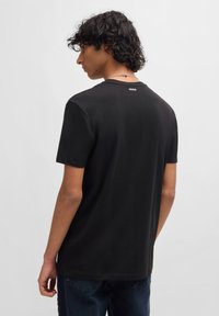 Tricou negru din bumbac cu guler rotund, mâneci scurte și un logo subtil "HUGO" pe spate, având o croială lejeră și o textură catifelată.
