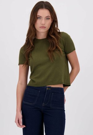 Olijfgroen cropped gebreide top met korte mouwen, ronde halslijn en geribbelde zoom, gecombineerd met donkerblauwe spijkerbroek met voorzakken.