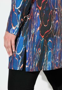 Dlouhý rukáv tunika s mnohobarevným abstraktním vzorem v modré, oranžové a černé barvě. Obsahuje boční rozparky a rovný lem, je zkombinována s černými legínami.