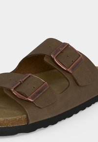 Sandale marron à bout ouvert avec deux brides réglables munies de boucles métalliques couleur cuivre et une semelle noire rainurée.