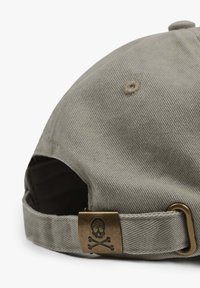 Khaki cotton cap with a curved brim, rear metal buckle featuring a skull and crossbones design, and textured fabric surface.