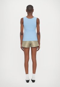 Svijetloplavi top bez rukava s rebrastim rubovima, uparen s metalik zlatnim šortsevima koji imaju teksturirani uzorak. Bijele čarape do članka i crne cipele.