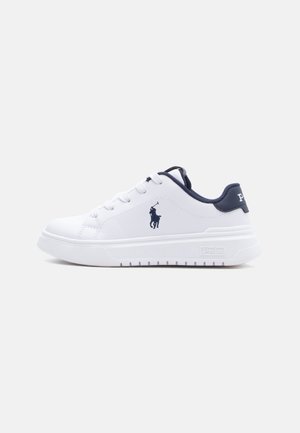 Baskets basses blanches avec logo et accents bleu marine, avec lacets et semelle blanche épaisse, vues de profil sur un fond uni.