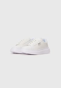 Sneakers bianchi con suola spessa e lacci, posizionati leggermente inclinati su uno sfondo bianco semplice.