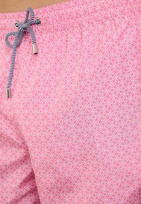 Różowe kąpielówki z okrągłym wzorem, z czarnym i białym pasem na sznurku w talii, wykonane z lekkiego, szybko schnącego materiału.