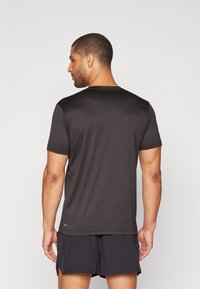 Camiseta negra de manga corta hecha de una tela suave, con cuello redondo y con el dobladillo trasero ligeramente alargado.