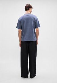 T-maica s kratkim rukavima, plava, od pamuka, ravnog kroja, uparena s crnim hlačama širokog kroja. Jednostavan dizajn s okruglim izrezom.