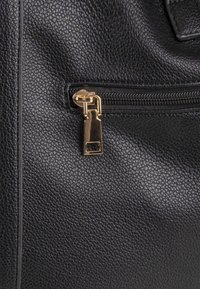 Zwarte leren tas met een gestructureerde oppervlakte, voorzien van gouden ritshardware en een rechthoekige ritstrekkeraanpassing.