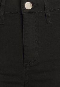 Jeans de mezclilla negra con una textura suave, que cuentan con un bolsillo frontal, costuras visibles y un cierre de botón metálico redondo.