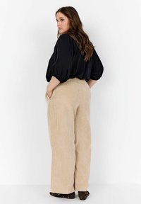 Top nero, ampia vestibilità con maniche a sbuffo abbinato a pantaloni larghi in corduroy beige a vita alta, con righe verticali e tasche laterali.