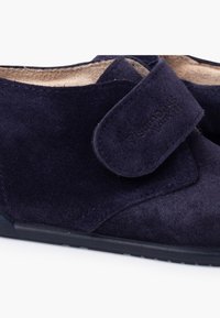 Chaussures en daim bleu marine avec une texture douce, dotées d'une fermeture à bande Velcro et d'une semelle en caoutchouc noir pour la stabilité.