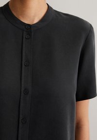 Schwarzes kurzärmeliges Hemd mit rundem Kragen, ausgestattet mit einer durchgehenden Knopfleiste und einer strukturierten Stoffoberfläche.