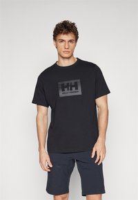Tricou din bumbac negru, cu guler rotund și mâneci scurte, având un logo mare Helly Hansen în culorile negru și gri pe față.