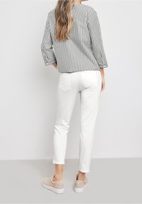 Top a rayas gris y blanco con mangas 3/4, combinado con pantalones ajustados blancos y zapatillas beige. La vista trasera muestra un corte relajado y un diseño sencillo.