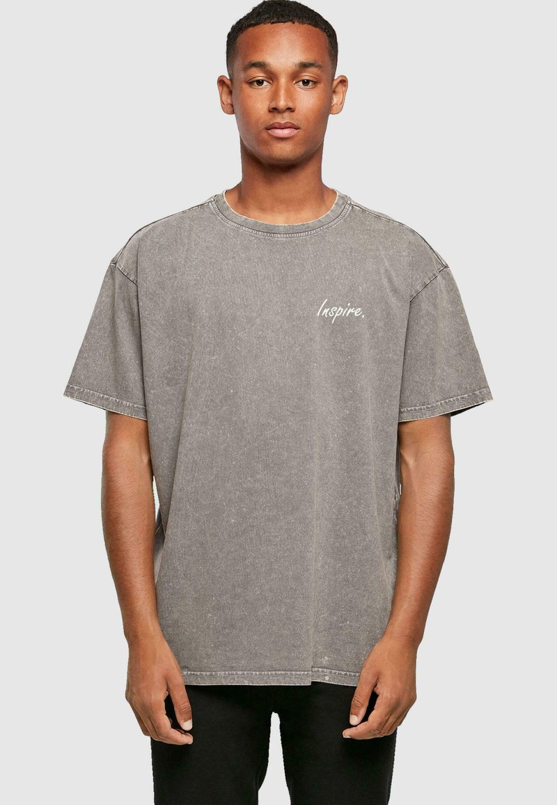 Camiseta de algodón gris con un corte holgado, cuello redondo y mangas cortas. Presenta el texto "Inspire." en blanco, con una textura desvanecida.