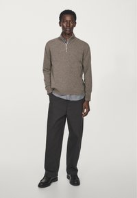 Pull gris zippé avec une finition texturée, porté par-dessus une chemise à col bleu clair, associé à un pantalon noir et des chaussures noires.