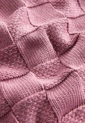 Strickdecke in sanftem Rosa mit einem strukturierten Gittermuster, das erhobene Quadrate und verschiedene Stricktechniken für zusätzliche Tiefe aufweist.