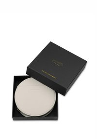 Okrągiwy, kremowy portfel skórzany w czarnym pudełku z złotym napisem. Portfel ma gładką teksturę i proste przeszycia.