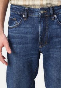 Jeans de mezclilla azul con una forma ajustada, que presentan un ligero desgaste, acentos de costura naranja y bolsillos frontales. Incluyen un cierre de botón y cremallera.