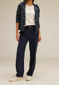 Marinblå vida byxor i kombination med en krämfärgad topp och en mörk läderjacka. Klädseln har en elegant design och mjuka texturer.