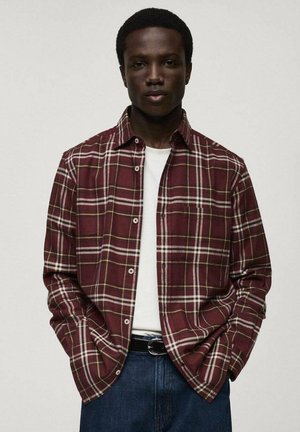 Camicia in flanella a quadri rossa e bianca con colletto, chiusura a bottoni e maniche lunghe, indossata sopra una t-shirt bianca, abbinata a jeans blu.