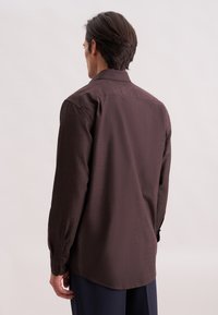 Camicia marrone a maniche lunghe con una texture sottile, polsini abbottonati e orlo curvo, vista da dietro.