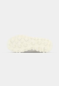 Såle av en sko med et robust, teksturert design med dype spor og heksagonale mønstre, hovedsakelig i off-white farge.