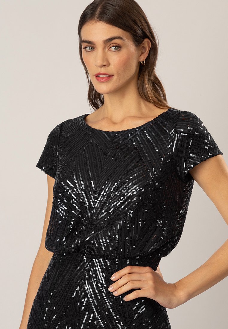 Une robe en sequins noire présente un design géométrique avec des manches courtes et une taille froncée, mettant en valeur une surface brillante et texturée.
