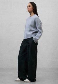 Light blue knitted sweater with ribbed hem, paired with loose black trousers and white sneakers, against a neutral background.