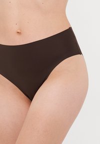 Woman wearing seamless dark brown bikini-style underwear, visible from waist to upper thighs against a plain background.