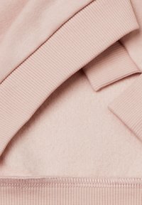 Felpa rosa chiaro con polsini e orlo a costine. Presenta un morbido tessuto interno spazzolato e un materiale esterno liscio. Strati visibili.