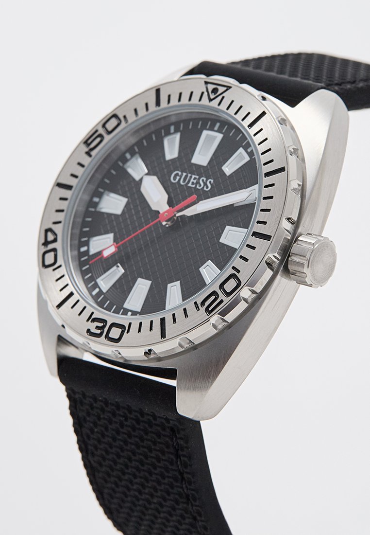 Reloj negro con caja de acero inoxidable, esfera negra texturizada, marcadores de horas blancos y segundero rojo. Cuenta con una correa de goma y un bisel giratorio.