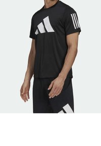 Camiseta atlética negra con un gran logo gráfico blanco en el frente y tres rayas blancas en la manga. Tela suave y ligera.