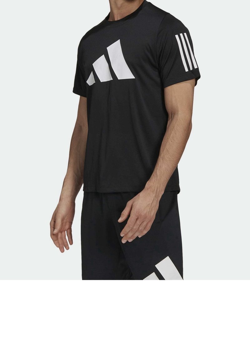 Camiseta atlética negra con un gran logo gráfico blanco en el frente y tres rayas blancas en la manga. Tela suave y ligera.