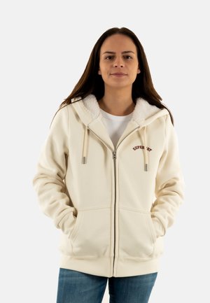 Felpa con zip color crema, con un interno morbido e texturizzato, cappuccio con cordino regolabile e tasche frontali. Presenta un logo ricamato rosso.