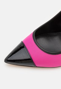 Escarpin à bout pointu avec bout en cuir verni noir brillant et partie supérieure en tissu rose vif avec bordure noire.