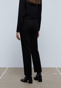 Suéter de punto negro y pantalones a juego, con un patrón texturizado. Los pantalones tienen un corte recto, combinados con botas de tobillo negras con tacón.