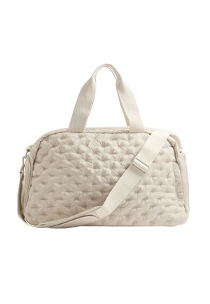 Sac de voyage en tissu matelassé beige avec deux poignées courtes et une bandoulière ajustable, sur fond blanc.