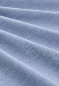 Jasnoniebieska tkanina z teksturowanym, falistym wzorem, z gładkimi liniami i subtelnymi przeskokami kolorów, tworząca miękki i płynny wygląd.