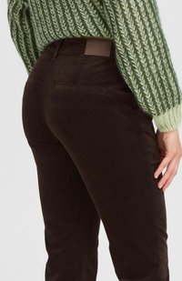 Braune Cordhosen mit schmalem Schnitt und Gesäßtaschen, kombiniert mit einem strukturierten grünen Strickpullover mit Rippenakzenten.