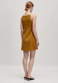 Ärmelloses Senfgelbes Kleid mit tailliertem Design, glatter Textur und einer Länge über dem Knie. Es zeichnet sich durch einen geraden Rücken und minimalen Nähten aus.