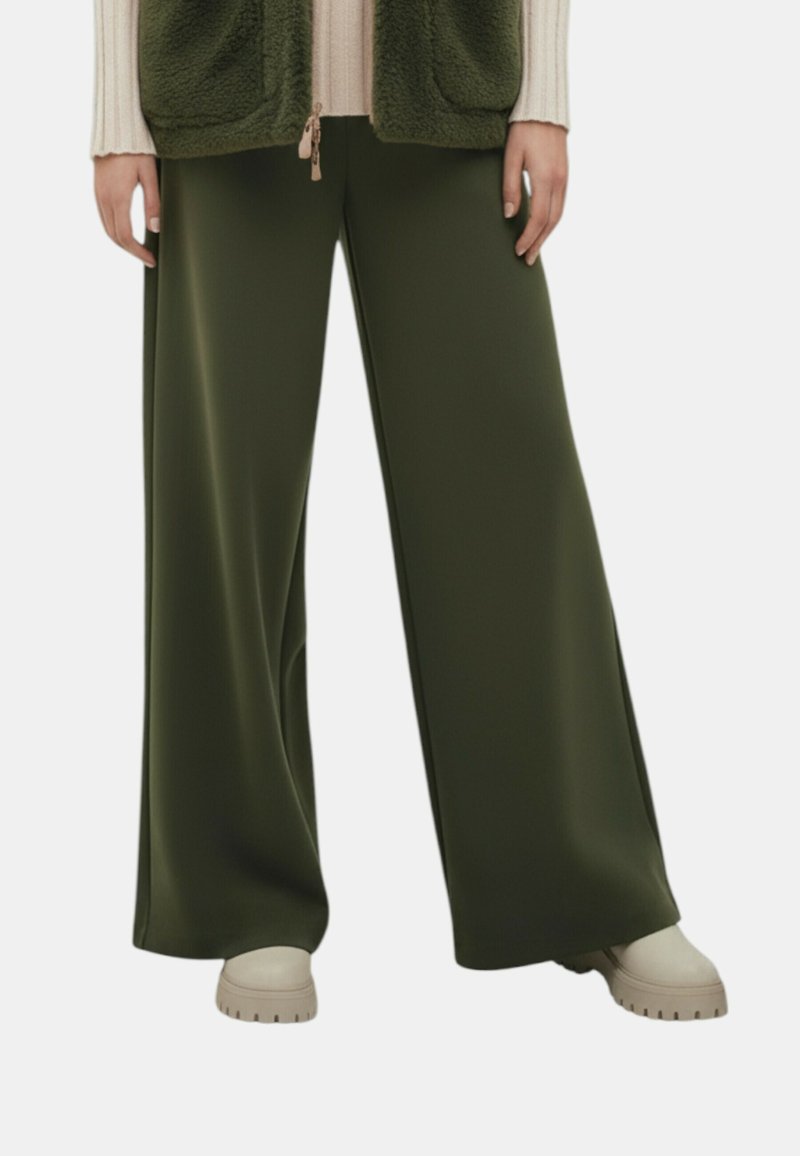 Wijd uitlopende broek in donker groene stof, gekenmerkt door een gladde textuur en een hoge taille. Gecombineerd met beige plateauzolen.