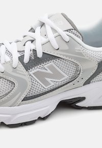 Lichte sneaker in grijs en wit, met een bovenwerk van mesh, rubberen zool, gestructureerde accenten en een prominente "N"-logo.