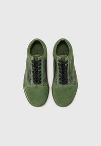Zapatillas de ante verde con cordones negros, costuras blancas y detalles oscuros en los laterales. Diseño de puntera redondeada y suela plana.