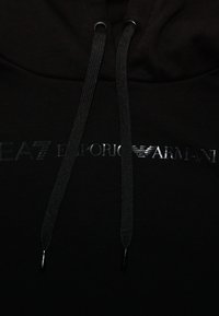 Sudadera negra con capucha que presenta un logo brillante de EA7 Emporio Armani en el frontal. Incluye cordones negros y una textura de tela suave.
