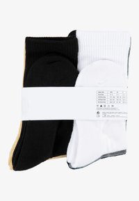 Tres pares de calcetines en negro, blanco y dorado, con textura acanalada y una etiqueta blanca que muestra la talla y las instrucciones de cuidado.