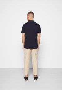 Námořnická polo košile s kontrastním límečkem, spárovaná se světle béžovými kalhotami a černými nazouvacími botami, pohled zezadu.